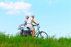 Älteres Paar fährt mit Fahrrädern über eine Wiese. 