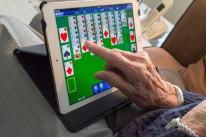 Älterer Mann spielt auf einem Tablet ein Kartenspiel, zu sehen sind das Tablet und eine Hand. 