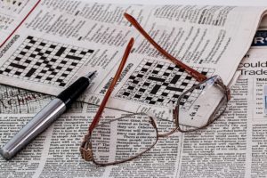 Zeitung mit Kreuzworträtsel, darauf liegen eine Brille und ein Kugelschreiber.