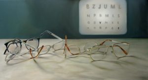 Brillen auf einem Tisch, an der Wand dahinter eine Optiker-Testtafel mit Buchstaben.